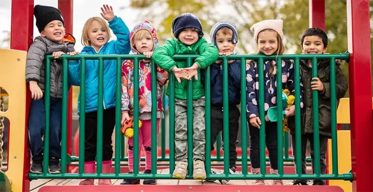 Group of happy children standing on a playground structure, smiling and playing outdoors.