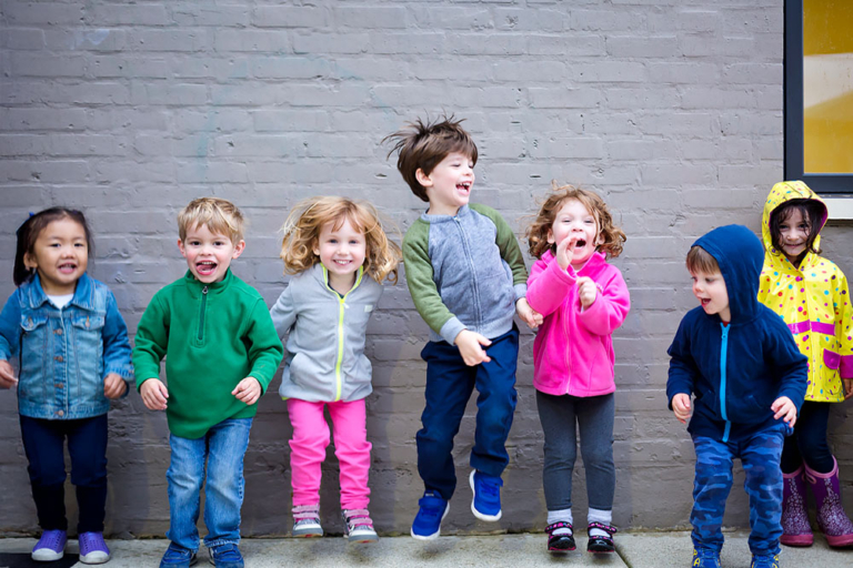 Young children stood in a line against the wall and jumping in the air