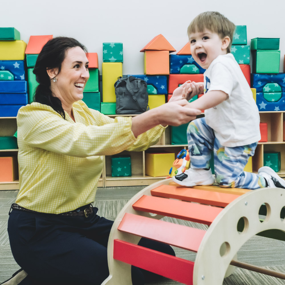 A young boy stood on a wooden play bridge holding hands with a woman
