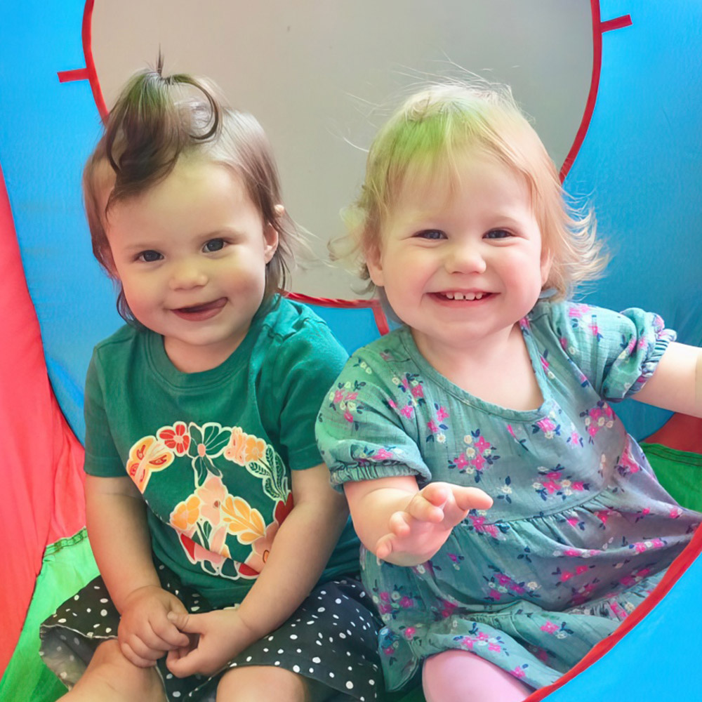 Two young children sat in a play tent and smiling into the camera
