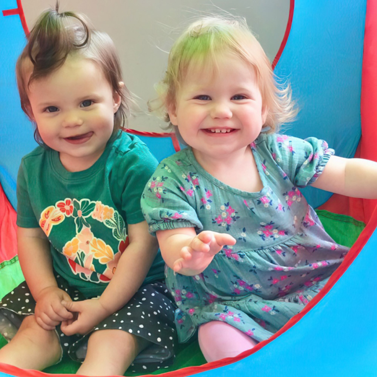 Two young children sat in a play tent and smiling into the camera