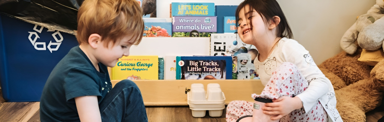 Two young children sat on the floor in front of a book shelf