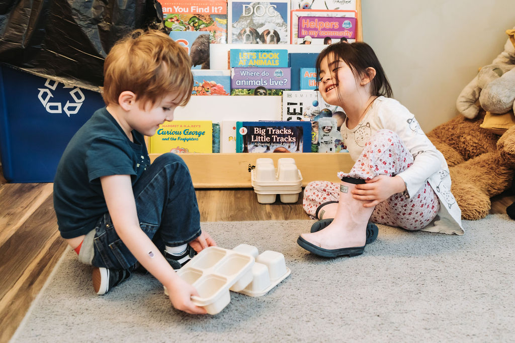 Two young children sat on the floor in front of a book shelf