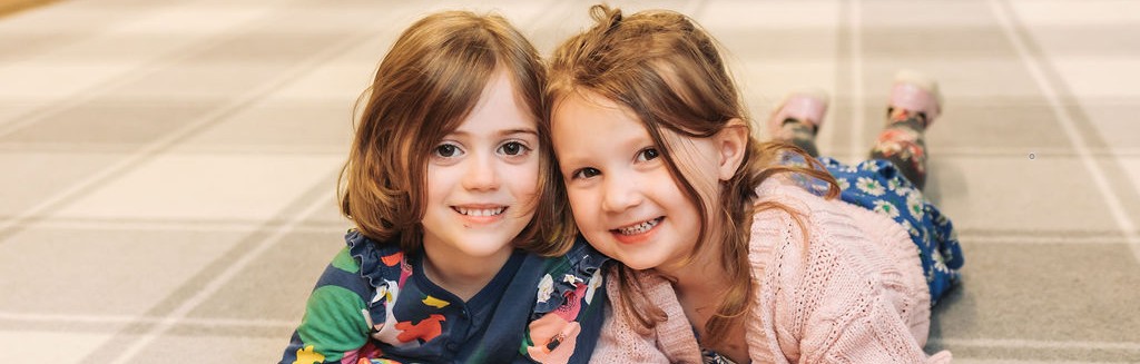 Two young girls lying on a carpet smiling into the camera