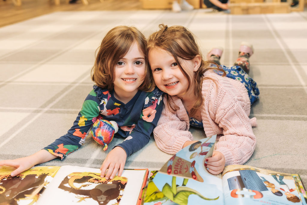 Two young girls lying on a carpet smiling into the camera
